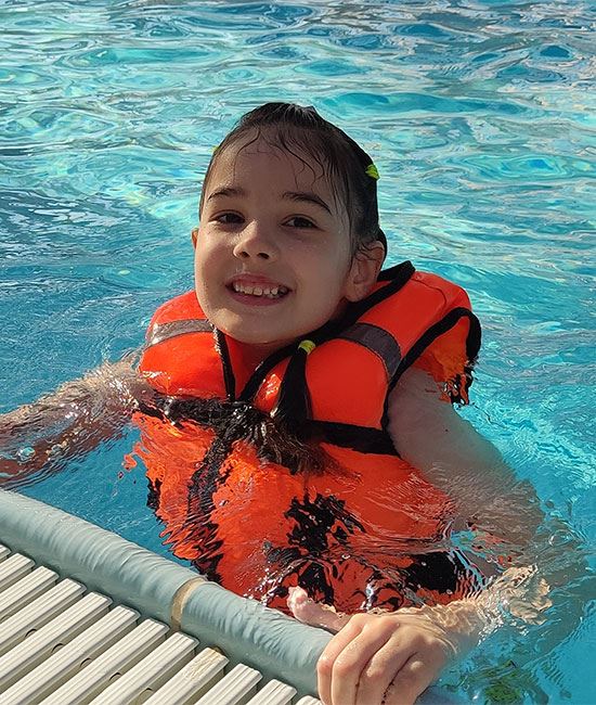 Child in swimming pool wearing life jacket.